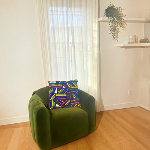 HD Decor Good Vibes square decorative pillow with colorful geometric pattern on a green velvet armchair by a window.
